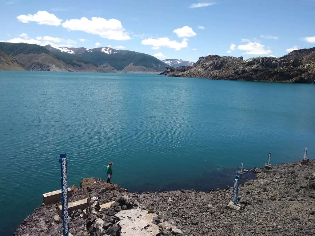 Limnímetros instalados en la ribera de una laguna altoandina de aguas turquesa, con un profesional de Rocks Geoconsulting en terreno